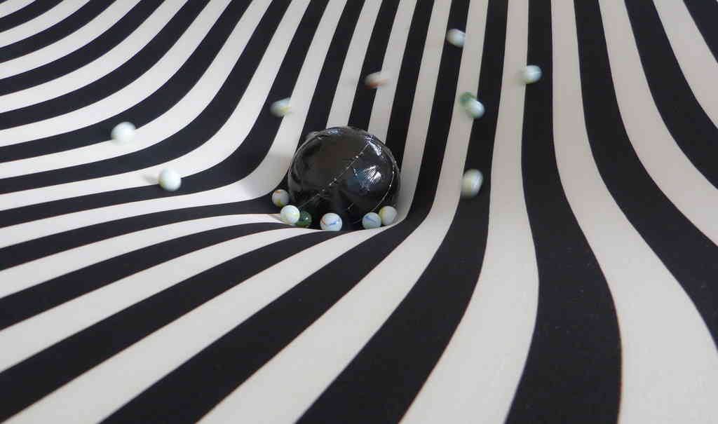 striped lycra sheet deformed by a heavy mass and marbles rolling around