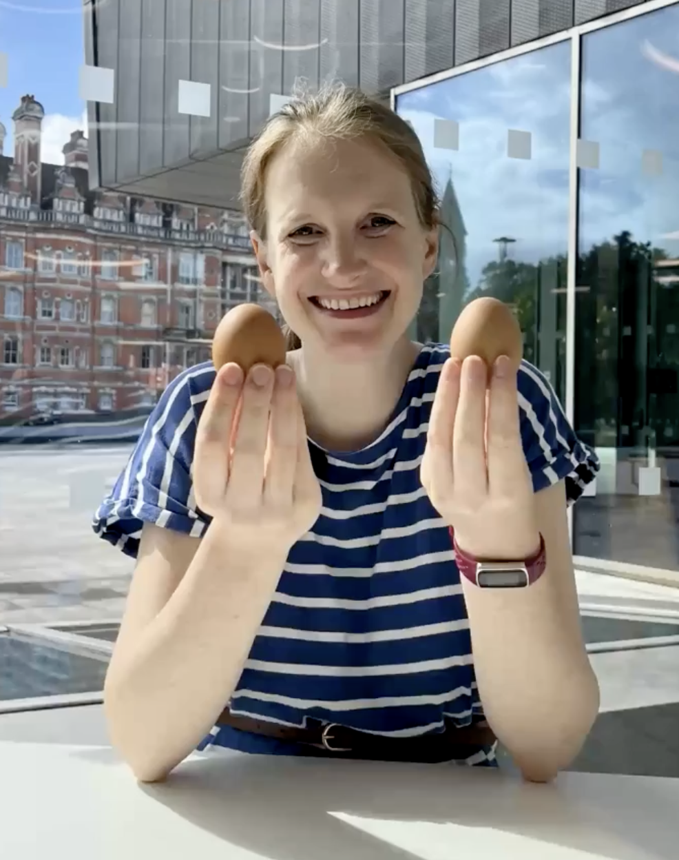 Vanessa Graber sitting on a desk holding two eggs in her
                        hands and smiling into the camera